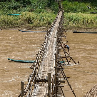 Wooden footbridge in Luang Prabang with a worker busy at its consolidation